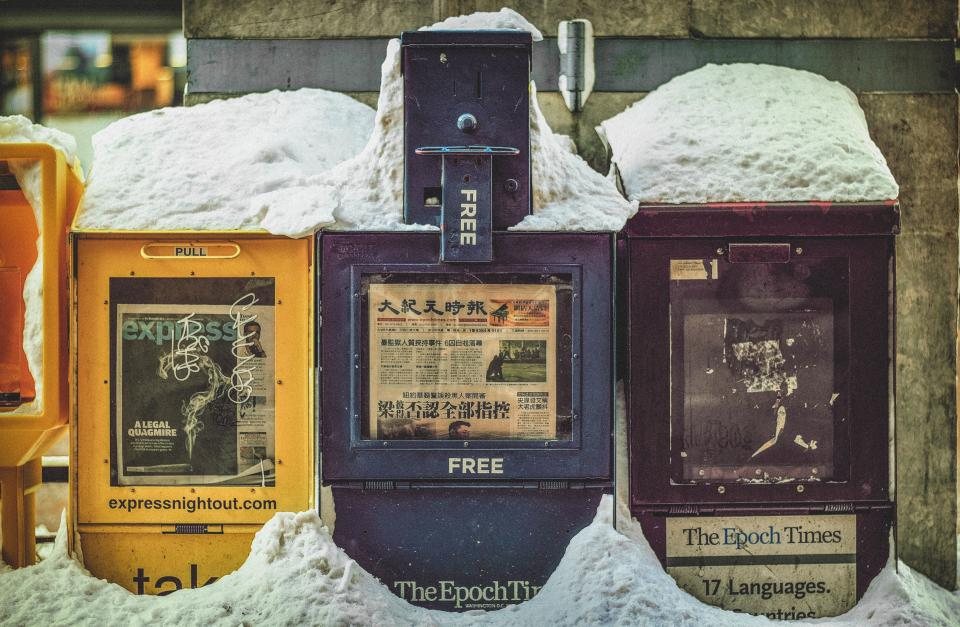 Worn newspaper boxes lined up along the curb