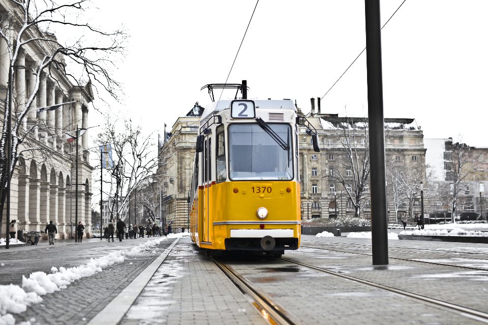 A yellow tram running down a street where the snow has melted