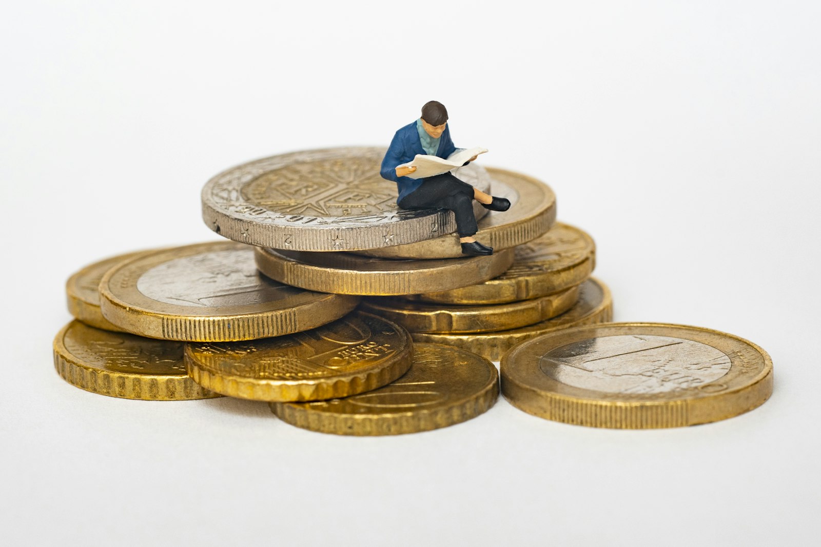 Small figurine sitting on a stack of coins reading a newspaper